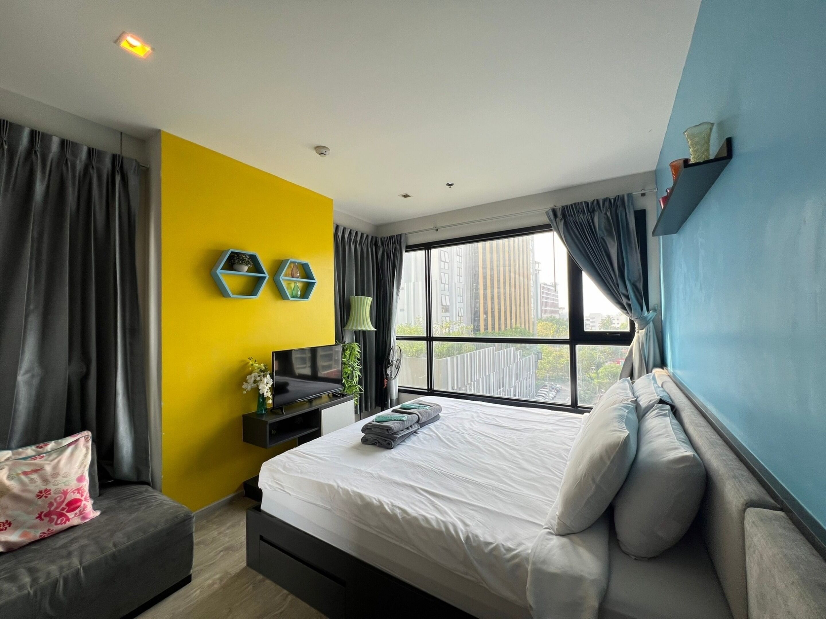 Een moderne slaapkamer met een bed, een sofa, een televisie en een raam met uitzicht op de stad.