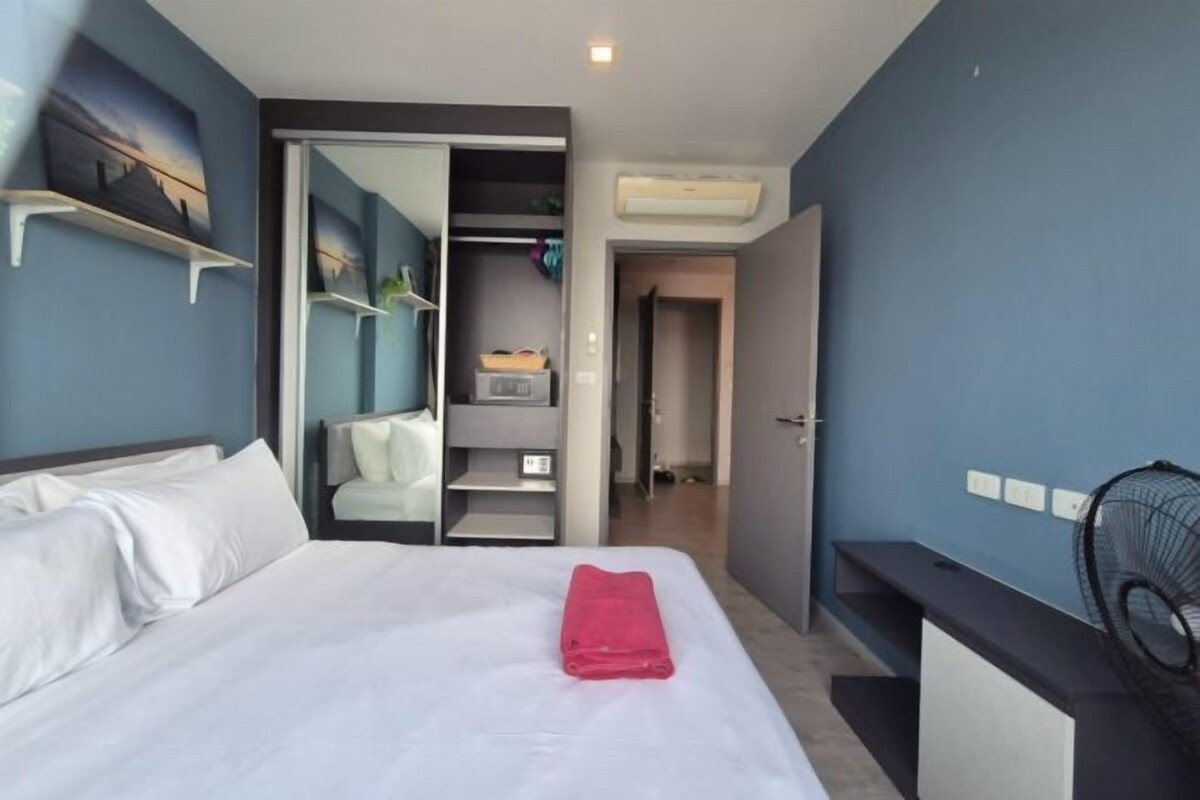 Une chambre d’hôtel avec un lit, une serviette rouge, une armoire et un ventilateur.