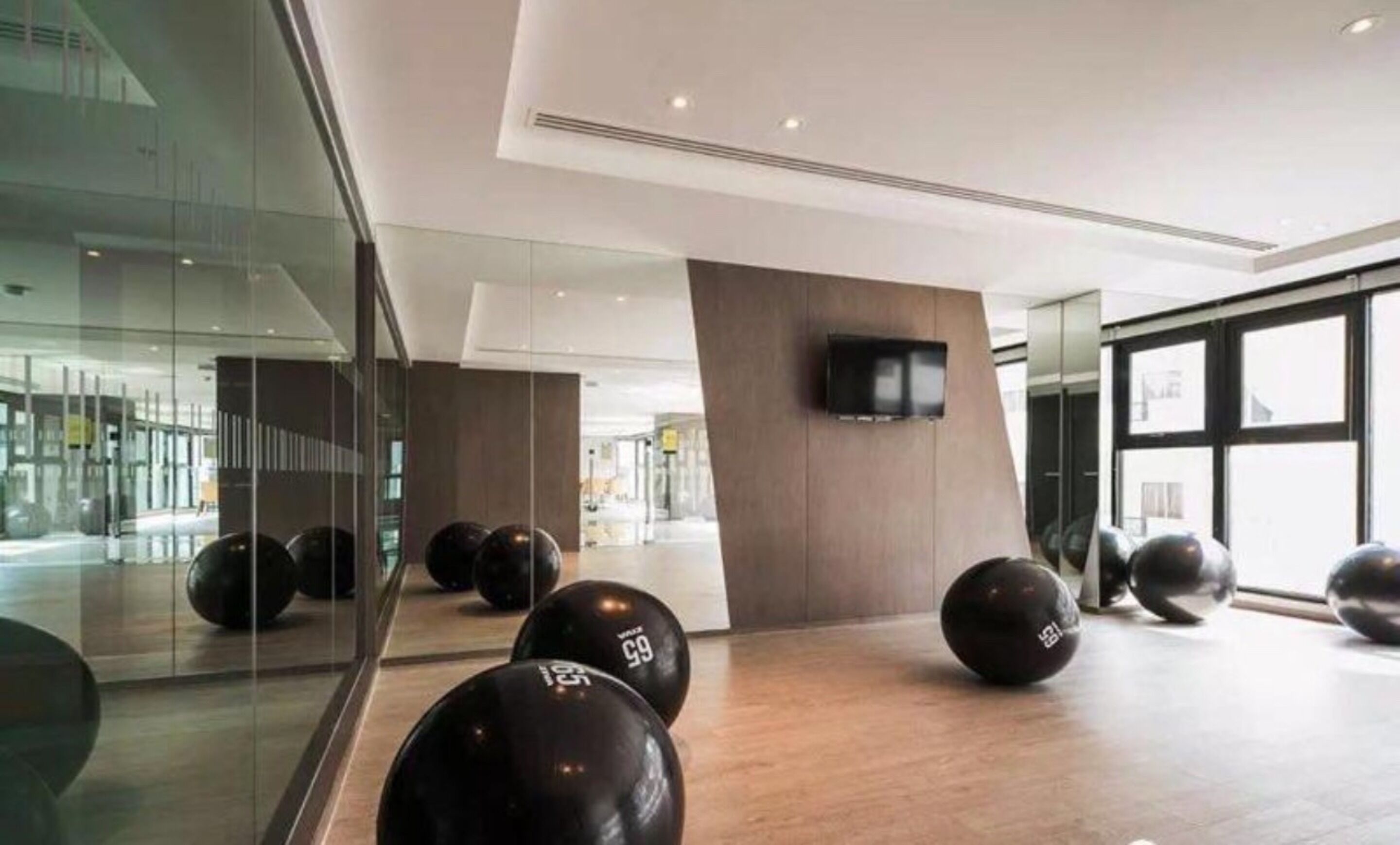 Un espace intérieur moderne doté d’un mur de verre qui reflète l’intérieur, d’un plancher en bois et de plusieurs ballons d’exercice noirs.