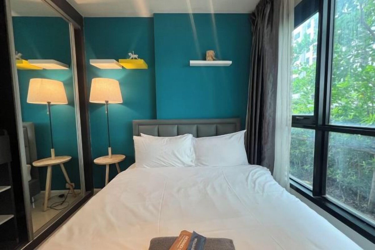 A hotel room with a large bed, two bedside lamps, a mirror, and a window with a view of greenery.
