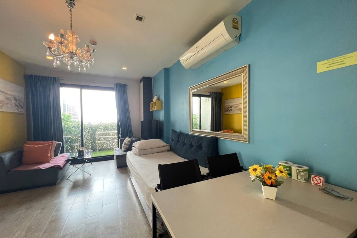 A hotel room with a bed, a dining table, a chandelier, an air conditioner, a mirror, and a balcony with curtains.