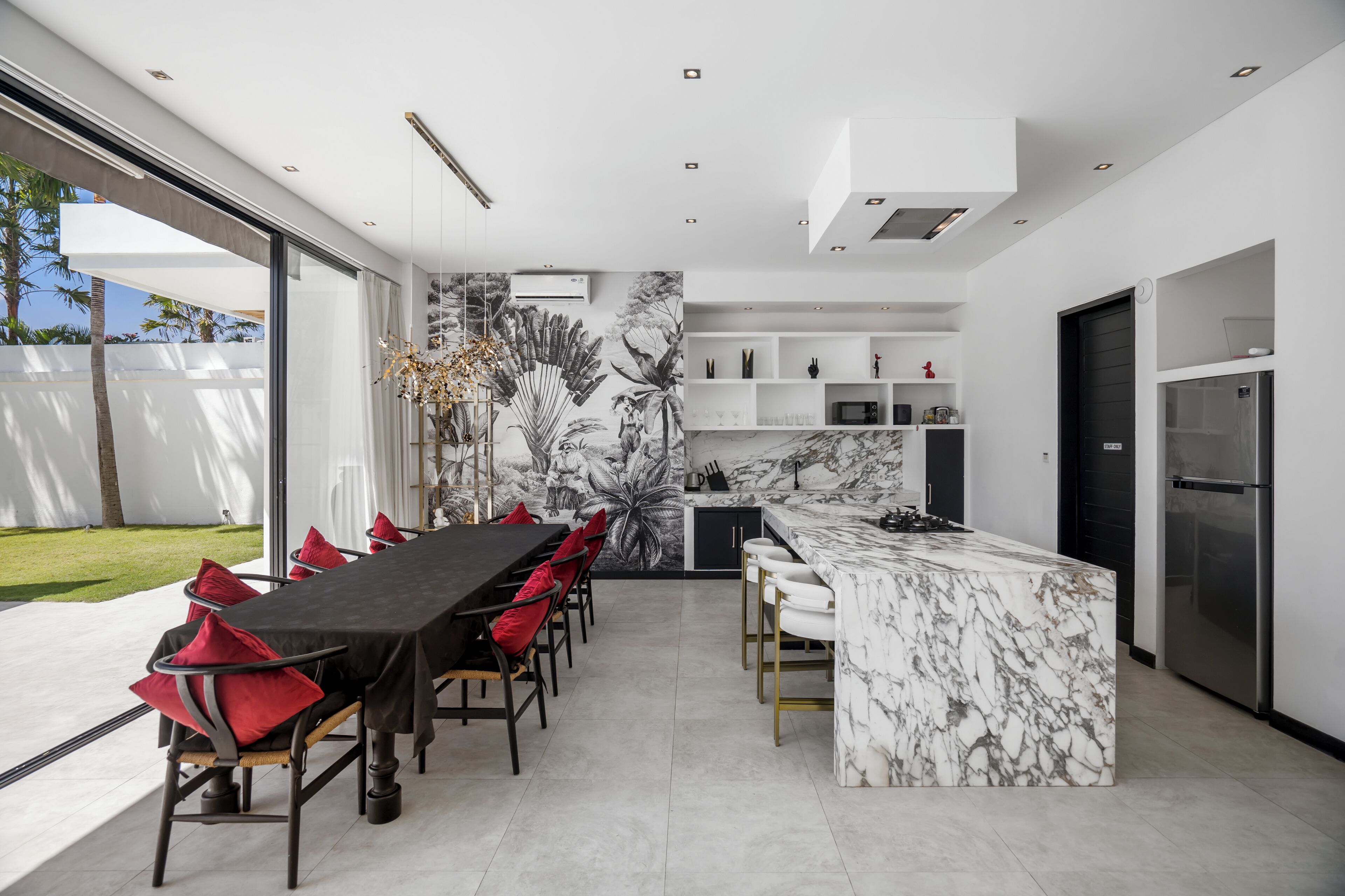 A modern kitchen with a marble island, a dining area with red chairs, and a view of the outdoors.