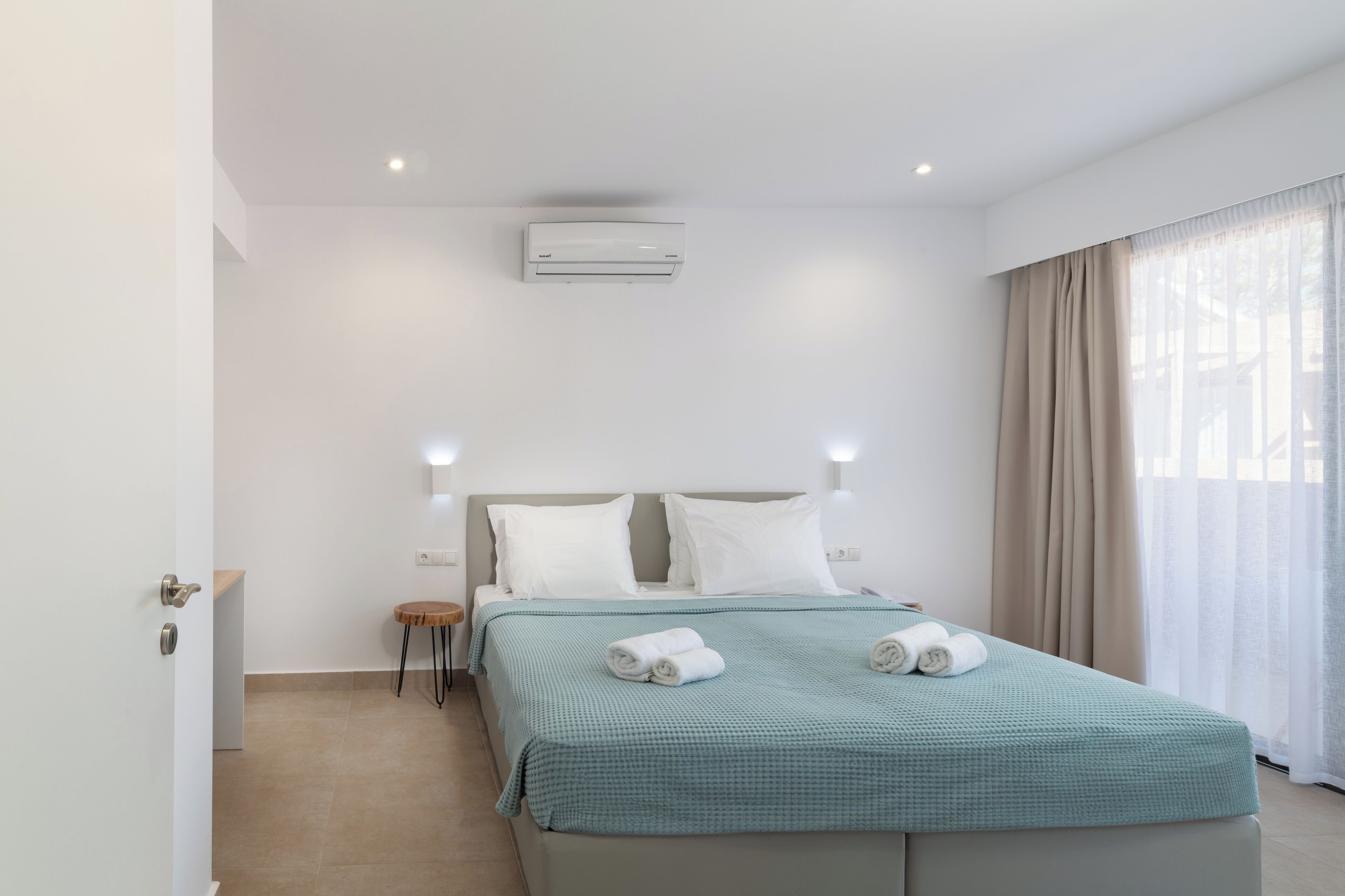 Una habitación de hotel con cama, mesita de noche, aire acondicionado y ventana con cortinas.