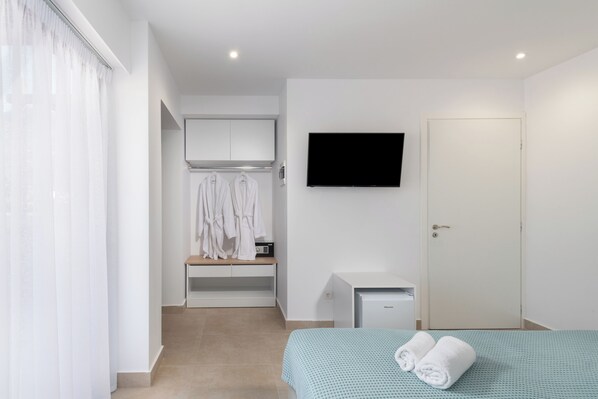 A hotel room with a bed, a TV mounted on the wall, a wardrobe, and a small desk with a chair. - Golden Bee Lifestyle (Hersonissos)