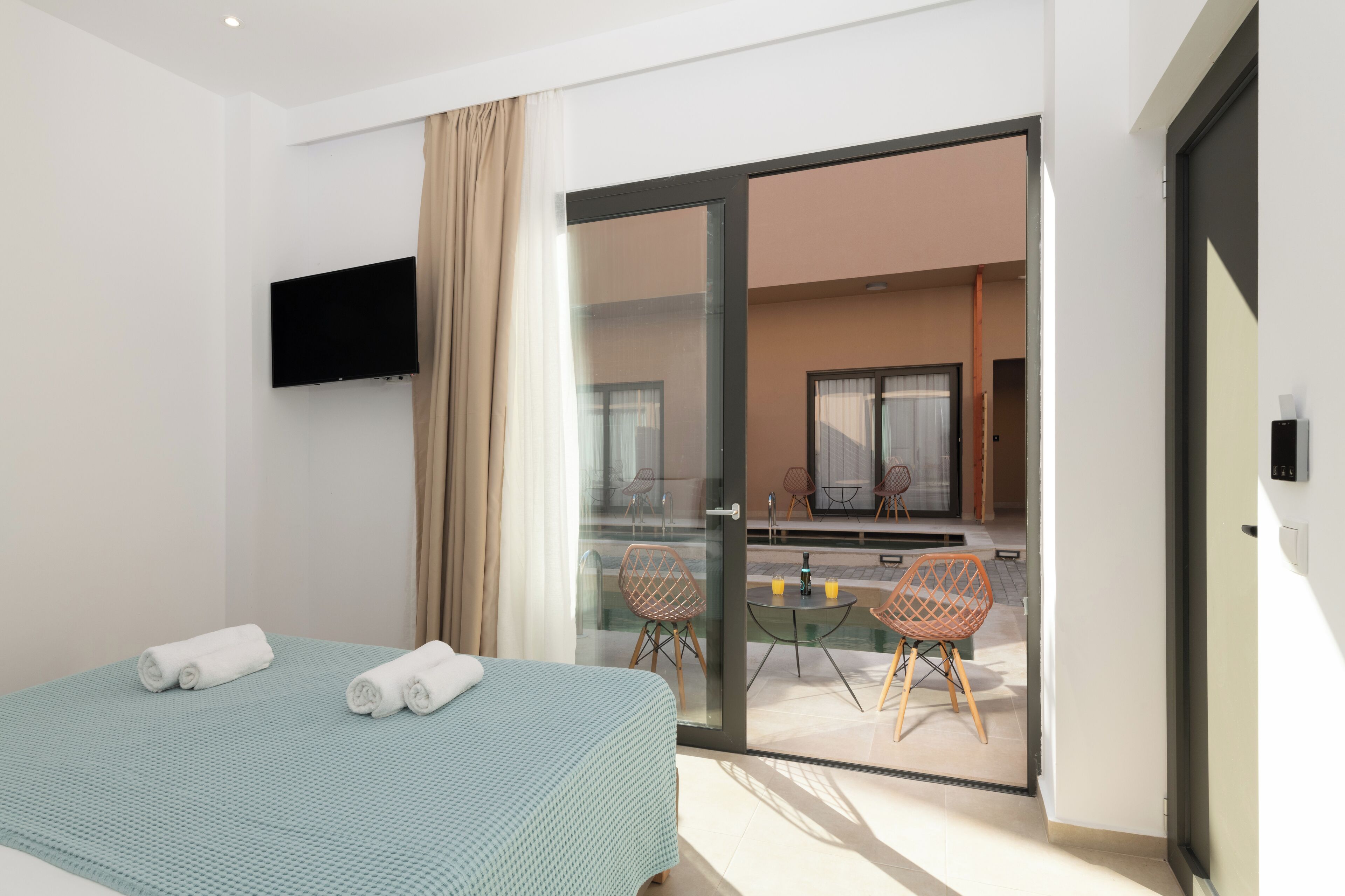 A modern hotel room with a bed, a flat-screen TV, and a balcony with chairs and a table.