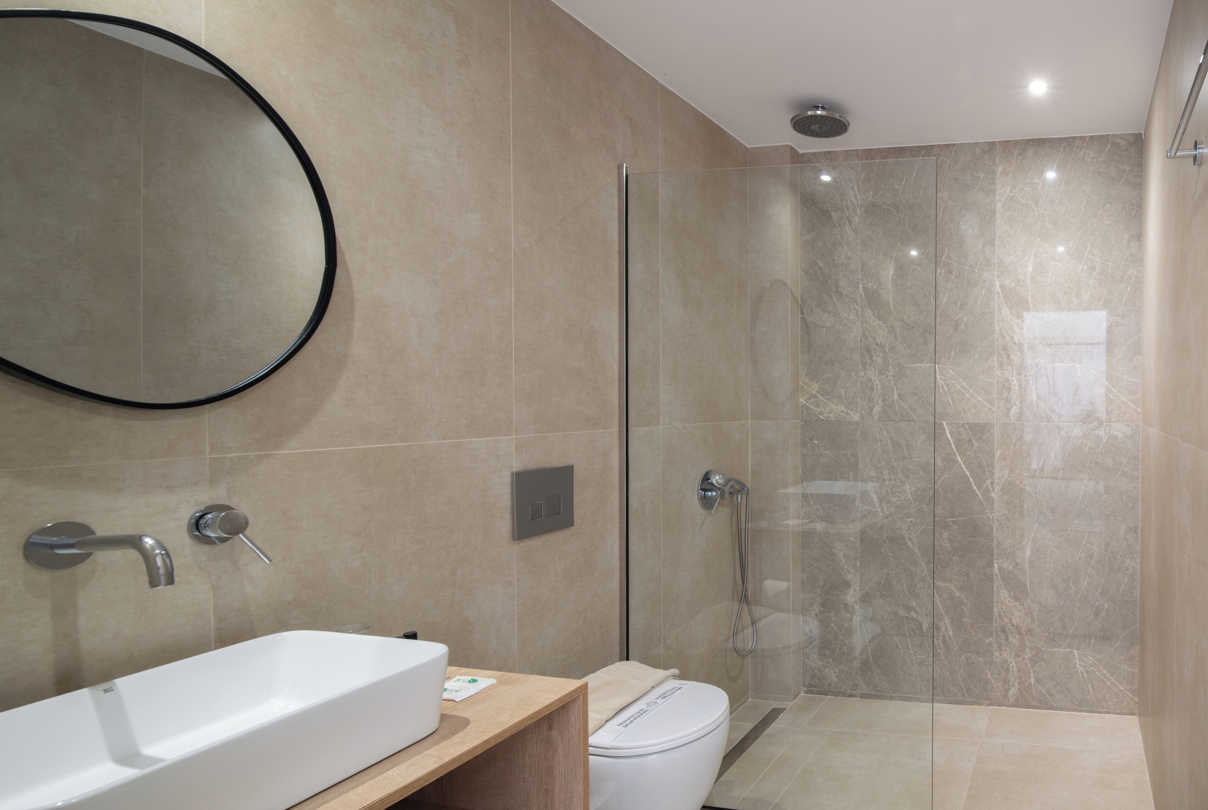 A modern bathroom with a large white sink, a round mirror, and a glass-enclosed shower.
