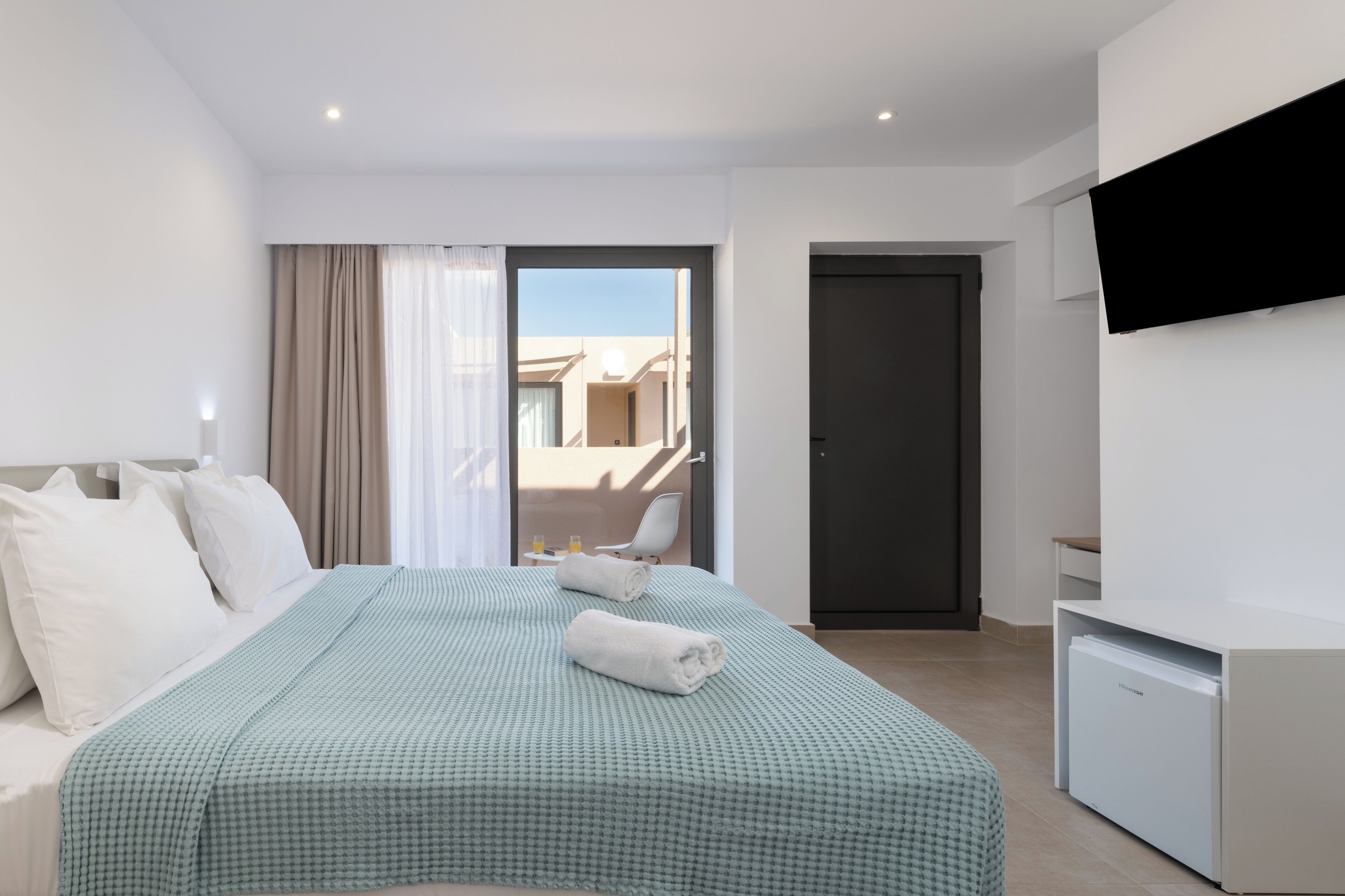 A hotel room with a bed, a TV mounted on the wall, a door, and a view of the outside.