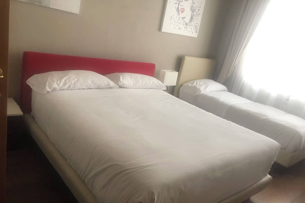 A hotel room with two beds, one with a red headboard and white bedding, and the other with white bedding. There is a painting on the wall above the beds.