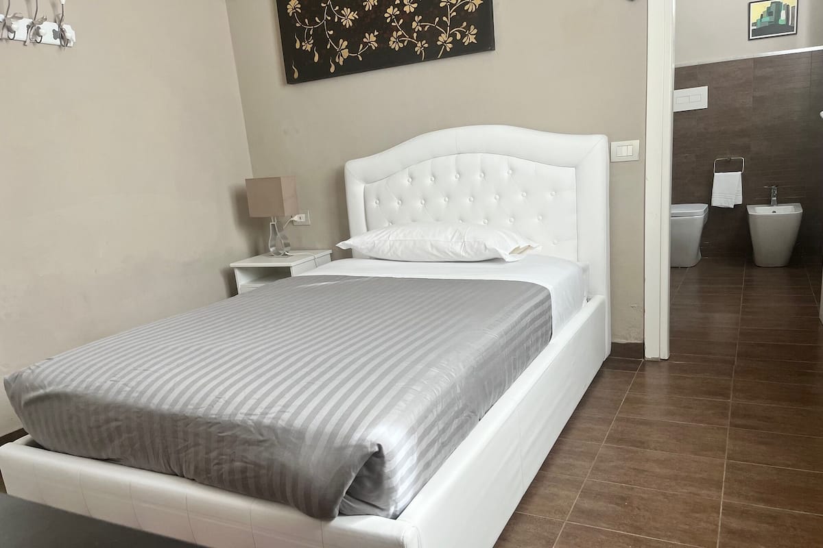 A neatly arranged hotel room with a bed, bedside table, lamp, and a wall-mounted artwork.