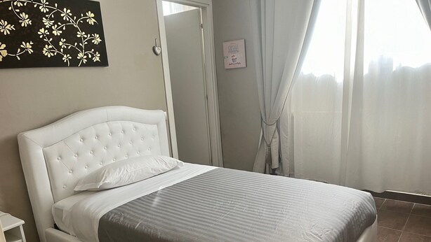 Una cama bien hecha, con cabecera blanca y ropa de cama gris, una mesita de noche pequeña y un adorno en la pared.