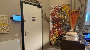 Una habitación con una puerta blanca, una pantalla digital, un cuadro abstracto de colores y un escritorio con un ordenador.