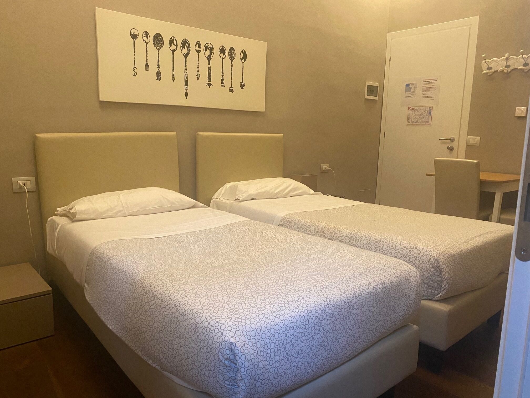 Een hotelkamer met twee bedden, een kunstwerk van sleutels aan de muur, een klein tafeltje en een stoel.