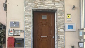 Una puerta marrón con fachada de piedra, un buzón, un casillero rojo y un cubo de basura metálico.