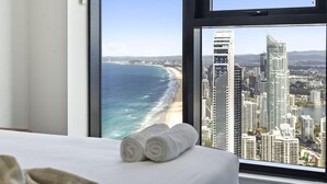 Une chambre d’hôtel dotée d’une grande fenêtre donnant sur une plage et sur le paysage urbain.