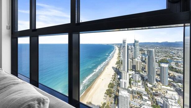Une chambre d’hôtel située dans un immeuble de grande hauteur, dotée d’une grande fenêtre offrant une vue sur la plage et le paysage urbain.
