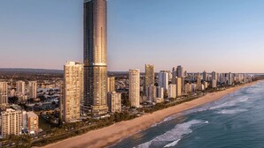 Un paysage urbain côtier avec de hauts immeubles, dont un gratte-ciel incurvé particulièrement imposant, une plage et un ciel dégagé.