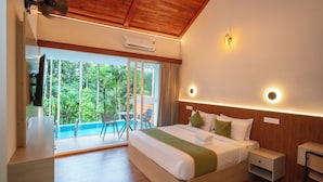 A modern hotel room with a large bed, a small desk, and a view of a swimming pool and greenery. - Theyila Wayanad (Sulthan Bathery)