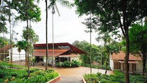 A hotel with a covered outdoor area, surrounded by lush greenery and palm trees. - Theyila Wayanad (Sulthan Bathery)