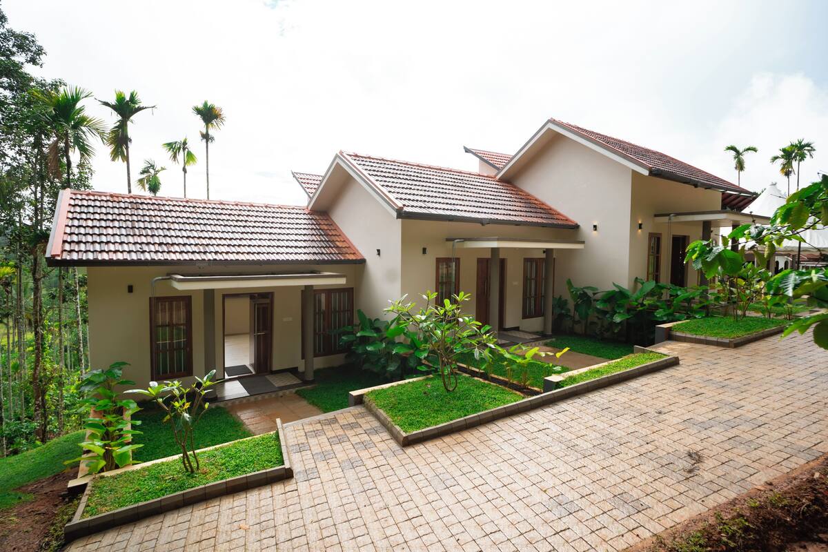 A two-story house with a tiled roof, a paved driveway, and a well-maintained garden with various plants and a small lawn area.