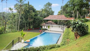 A swimming pool with a tiled deck, surrounded by lush greenery and tall palm trees. - Theyila Wayanad (Sulthan Bathery)