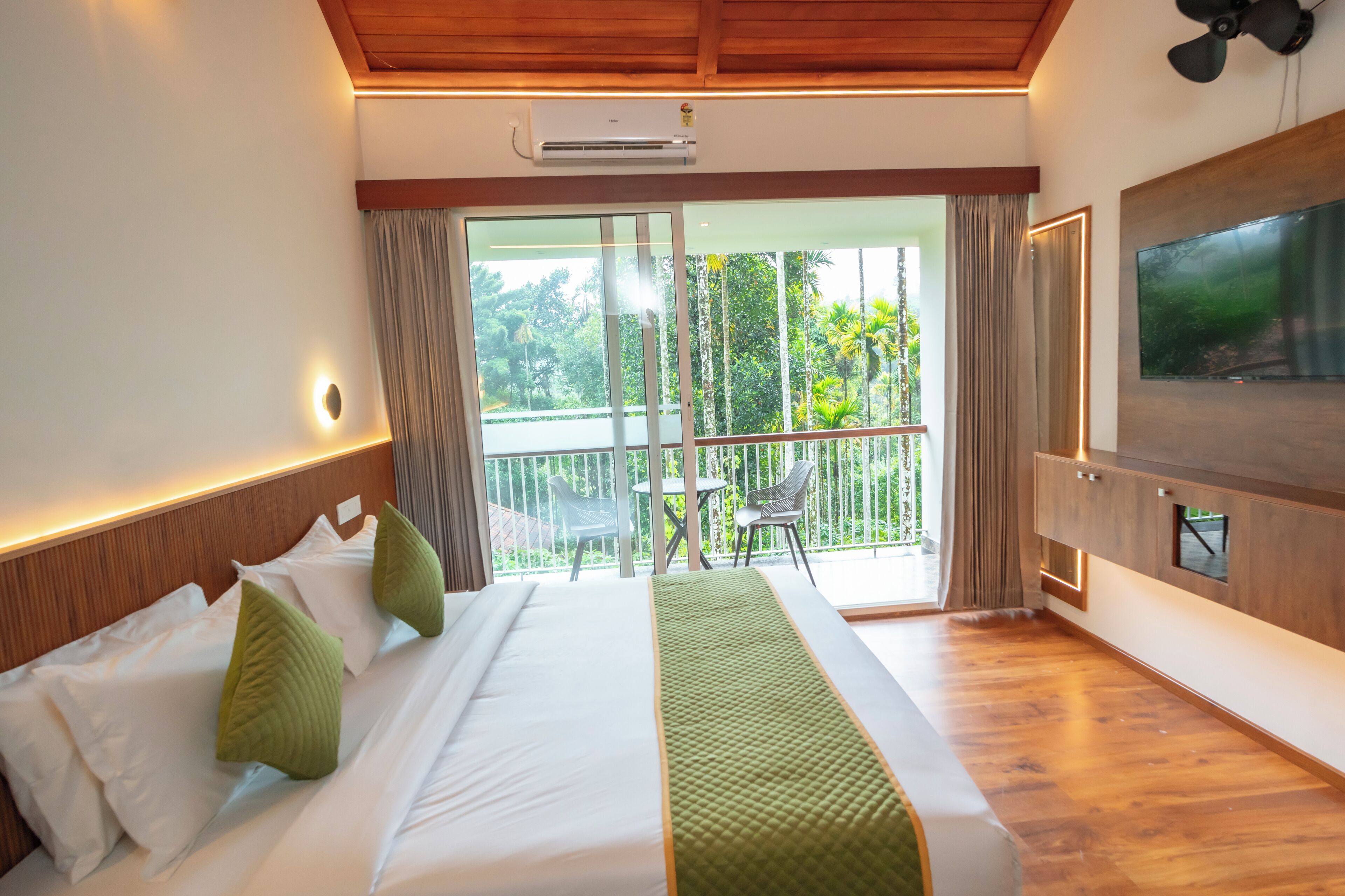 Une chambre d’hôtel avec un lit, une télévision, un balcon donnant sur un espace verdoyant et un ventilateur de plafond.