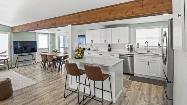 A modern kitchen with white cabinets, a stainless steel refrigerator, and a dining area with a wooden table and chairs. - Honeoye Lake | Hot Tub | Kayak | Fire Pit (Honeoye)