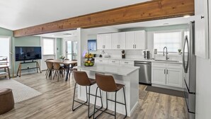 A modern kitchen with white cabinets, a stainless steel refrigerator, and a dining area with a wooden table and chairs. - Honeoye Lake | Hot Tub | Fire Pit (Honeoye)