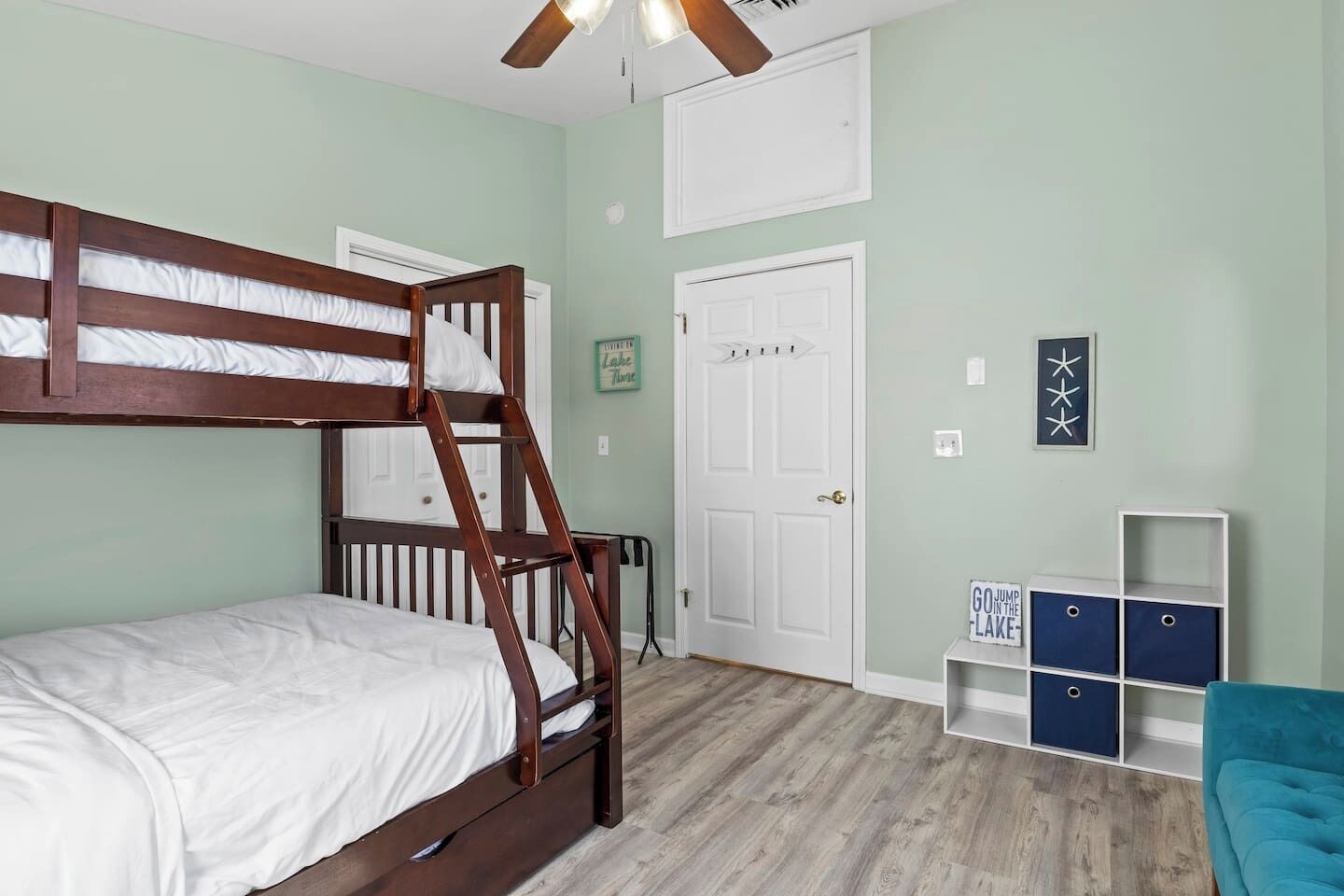 Un dormitorio con literas, una puerta blanca, un ventilador de techo y un pequeño armario azul.
