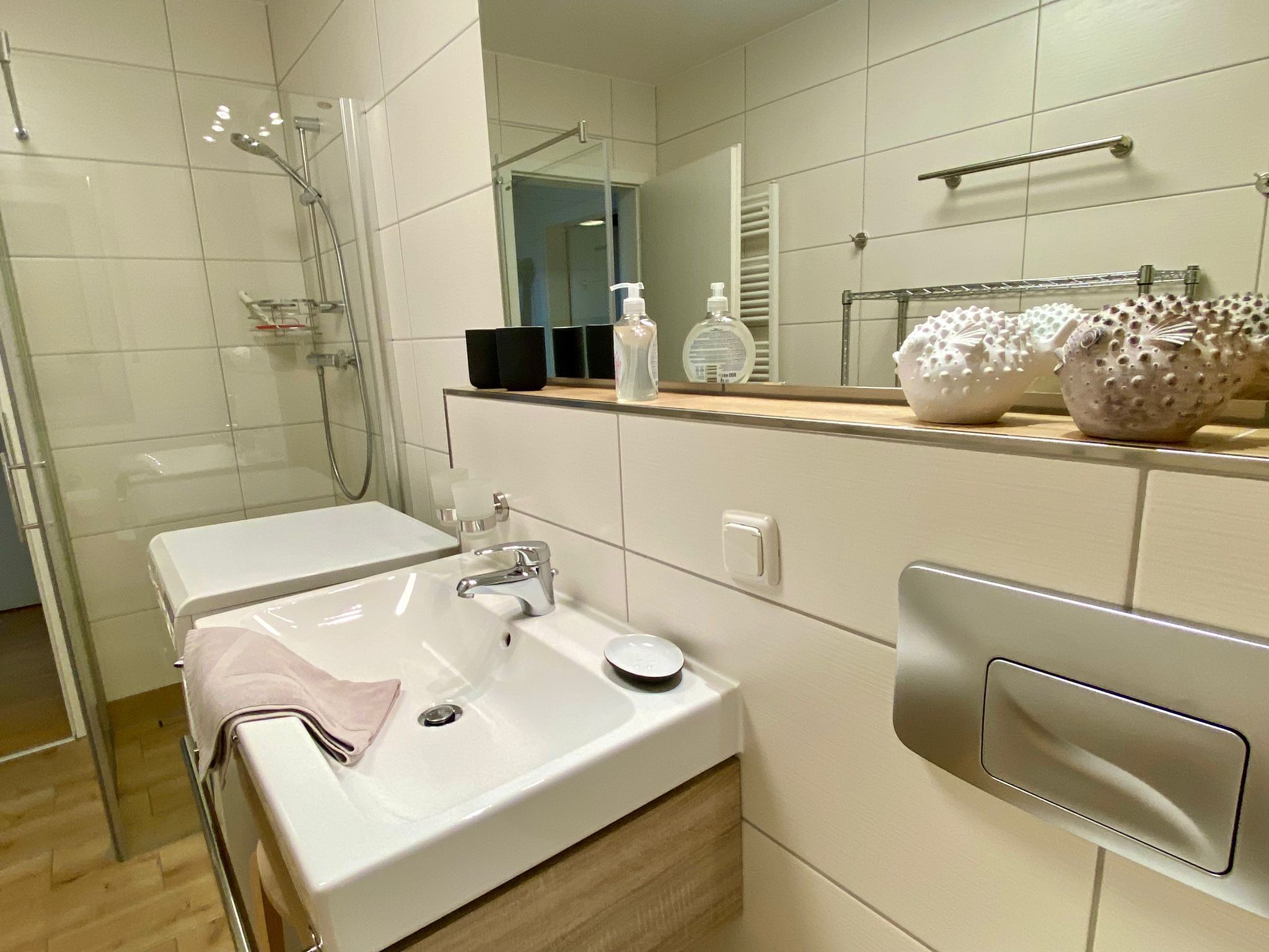 Une salle de bain moderne avec un lavabo blanc, une douche en verre et un miroir doté d’un porte-serviettes.
