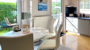Une cuisine moderne avec des meubles blancs, un coin repas doté d’une table ronde et de chaises, et une vue sur l’extérieur grâce à de grandes fenêtres.