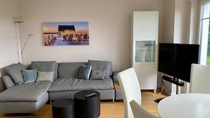 Un salon moderne avec un canapé d’angle, un téléviseur à écran plat, une table à manger et un tableau accroché au mur.
