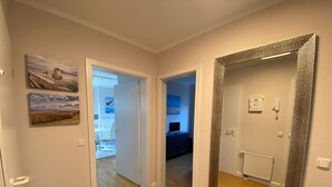 Un couloir doté d’un plancher en bois, d’un grand miroir avec un cadre à motifs, et de deux portes donnant sur des pièces différentes.