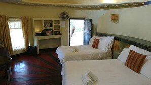 Una camera d'albergo con due letti, una scrivania con una sedia, un ventilatore e una finestra con tende.
