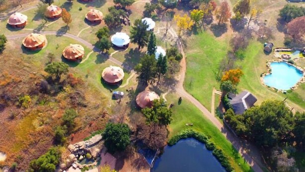 Vista aerea di un resort con diversi edifici a forma di cupola, una piscina e un piccolo lago.