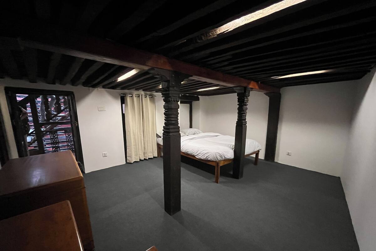 A room with a four-poster bed, a wooden desk, and a window with curtains.