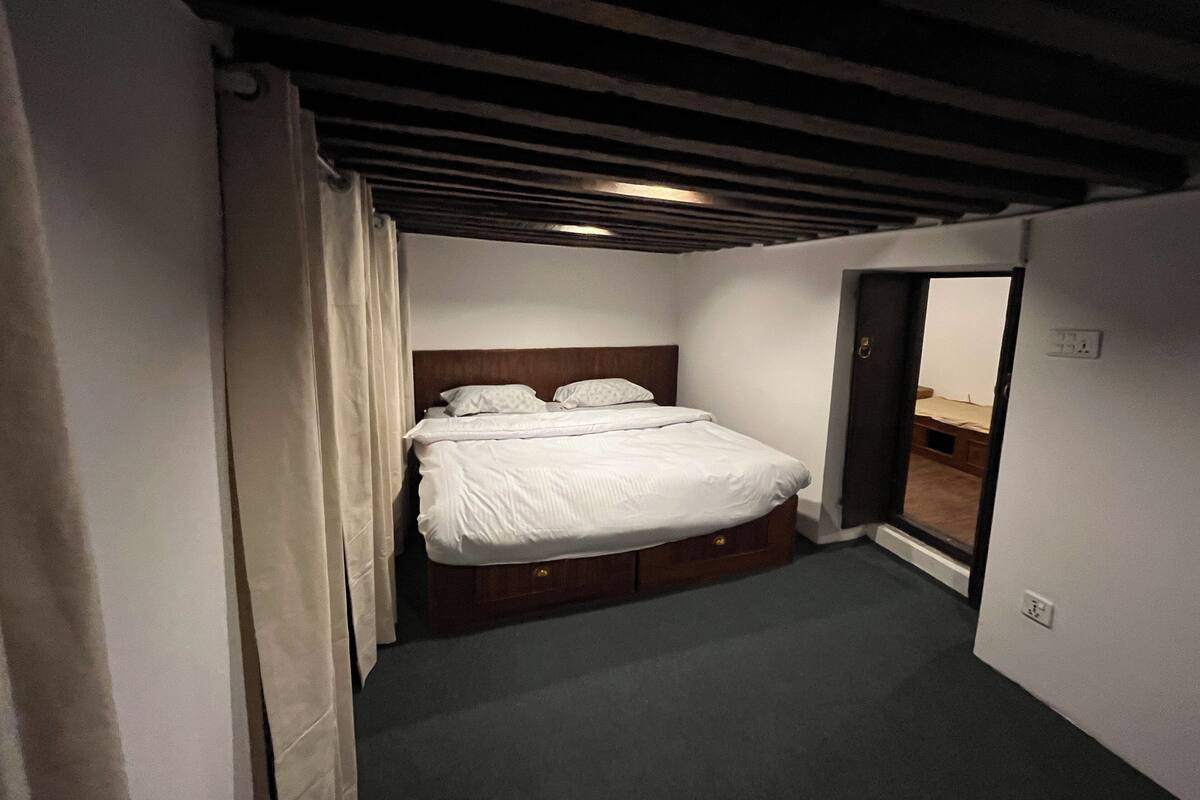 A small, dimly lit bedroom with a single bed, a wooden headboard, and a dark ceiling.