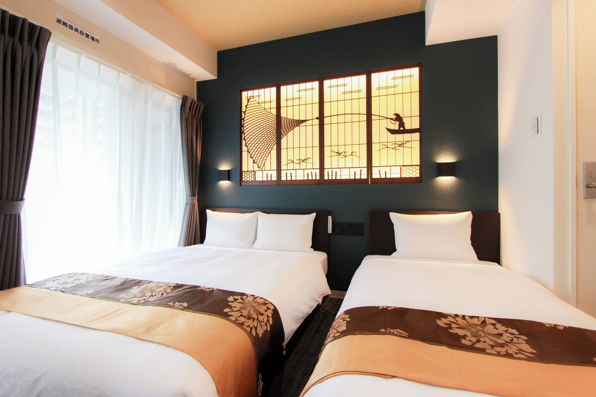 Une chambre d’hôtel avec deux lits, une grande fenêtre avec des rideaux et un élément décoratif mural.