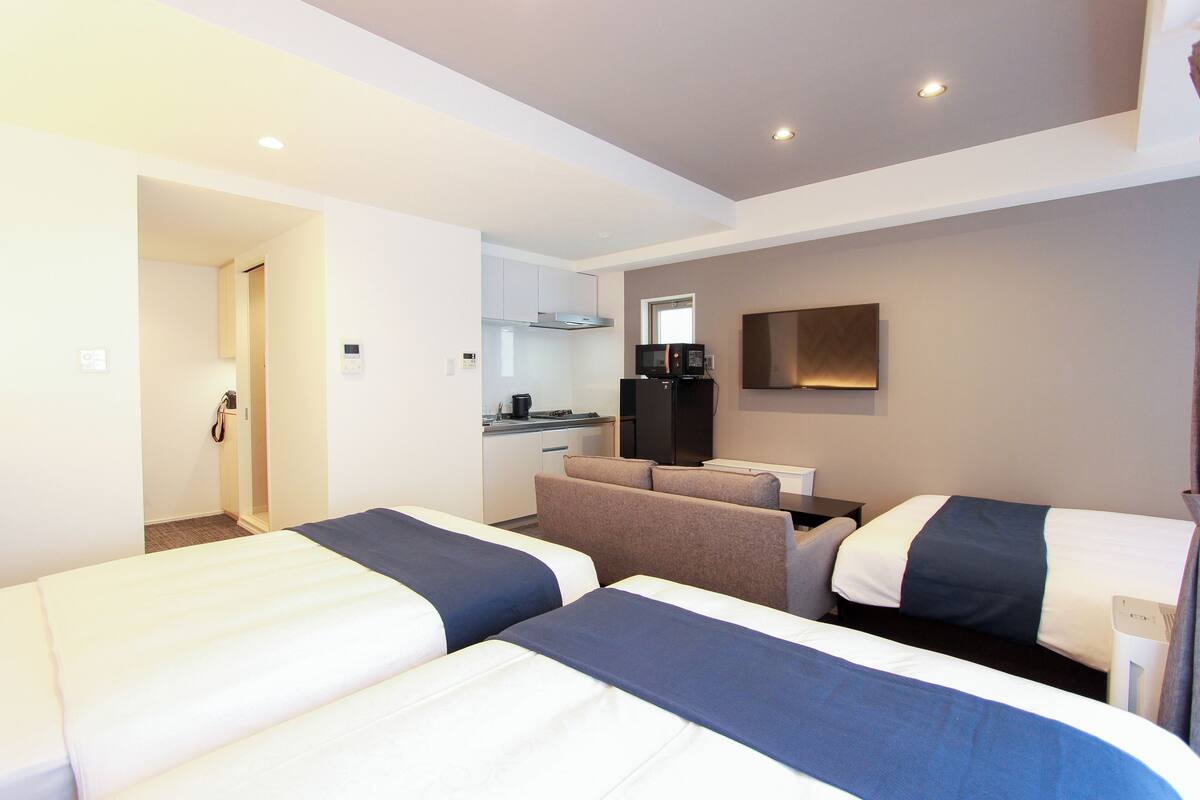 Une chambre d’hôtel avec deux lits, une kitchenette, un coin salon et un téléviseur.