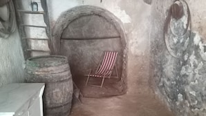 Una habitación pequeña y rústica con chimenea de piedra, una escalera de madera y un sillón a rayas.