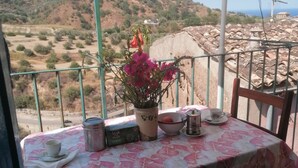 Una mesa con mantel floral, una planta en maceta con flores rosadas y un paraguas a rayas.