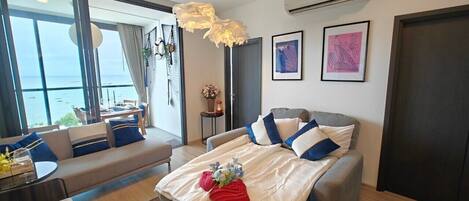 A modern hotel room with a large bed, a sofa, a dining area, and a view of the sea.