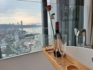 Une vue sur la ville depuis une chambre d’un immeuble de grande hauteur, avec une baignoire, une rose et une bouteille de vin sur un plateau.