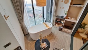 A modern bathroom with a freestanding bathtub, a round table with a vase, and a view of the city through large windows. - Edge Central Pattaya by Mickey (Pattaya)
