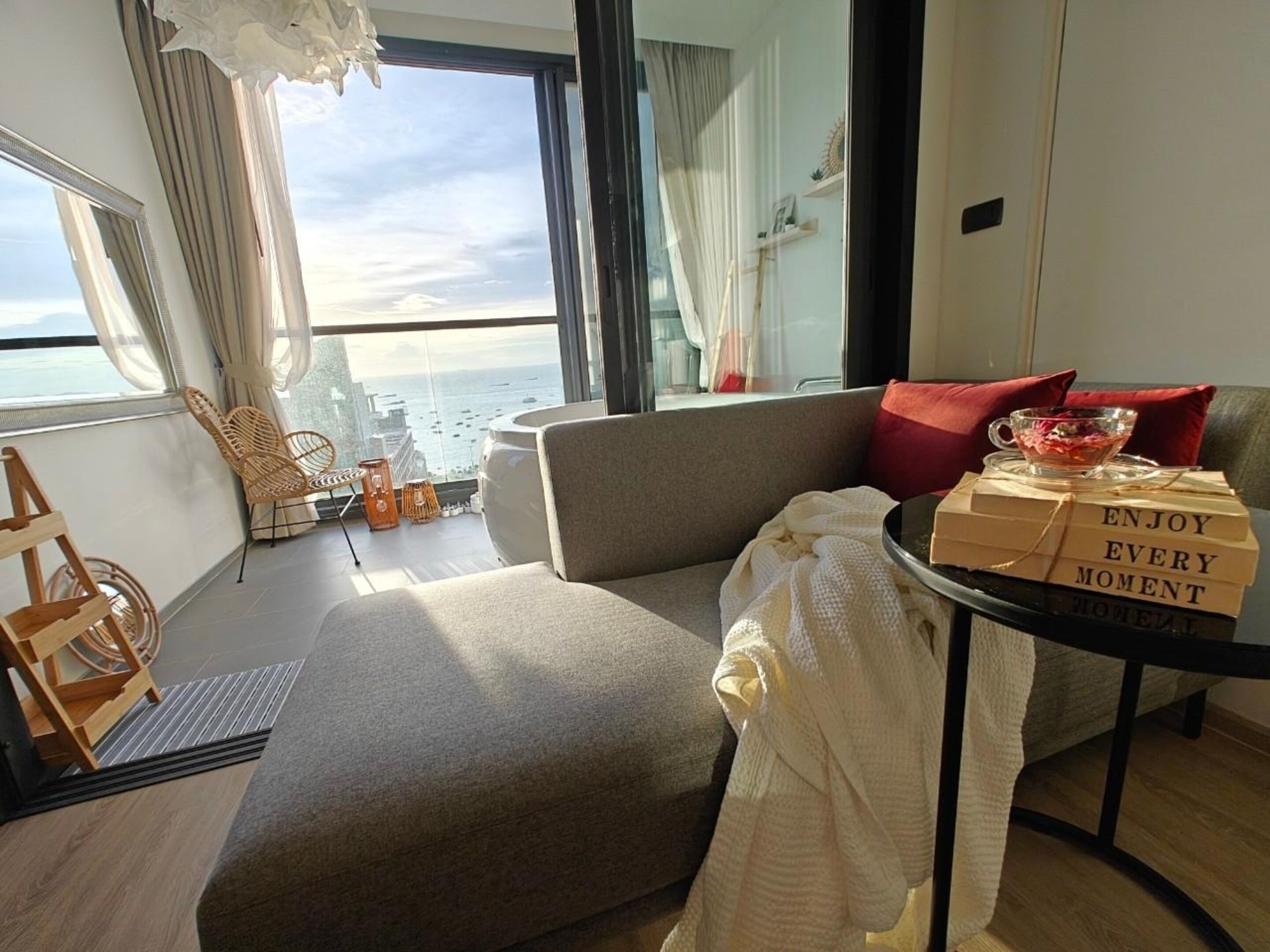 A modern living room with a sofa, a small table with a glass, and a view of the ocean.