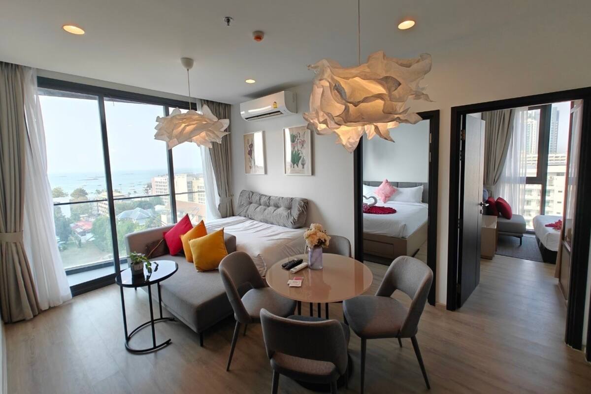 A modern hotel room with a large balcony, a round dining table, and a comfortable seating area.