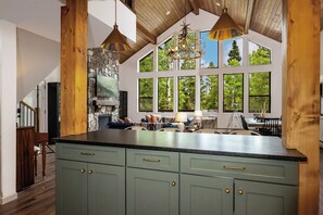 A spacious kitchen with a large island, stone fireplace, and large windows offering views of the outdoors. - Kids toys/games, cribs, play space, stone fireplace, decks (Angel Fire)
