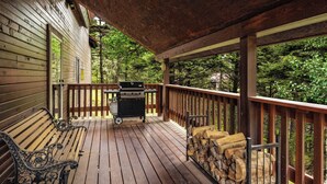 Una terraza de madera con una parrilla, bancos y vistas a un bosque.