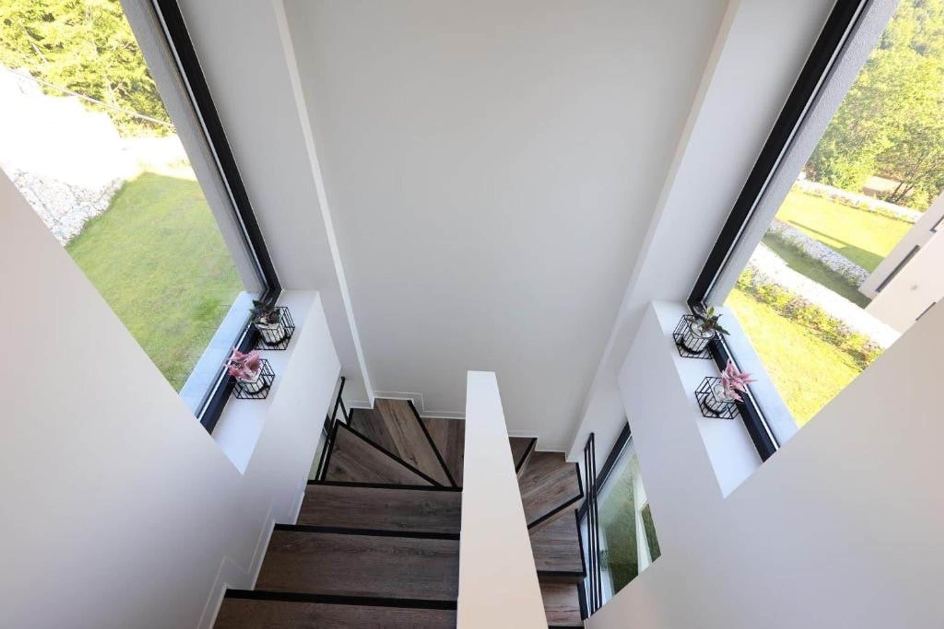 A modern staircase with wooden steps and glass railings, leading to a bright interior space.