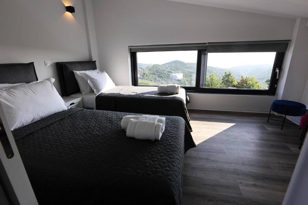 Habitació d'hotel moderna amb dos llits, un finestral gran amb vista a la muntanya i una cadira blava petita.