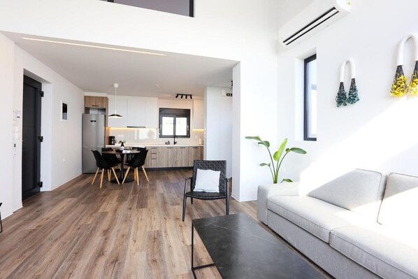Una sala de estar moderna con un sofá, una mesa de comedor con sillas y una cocina al fondo.